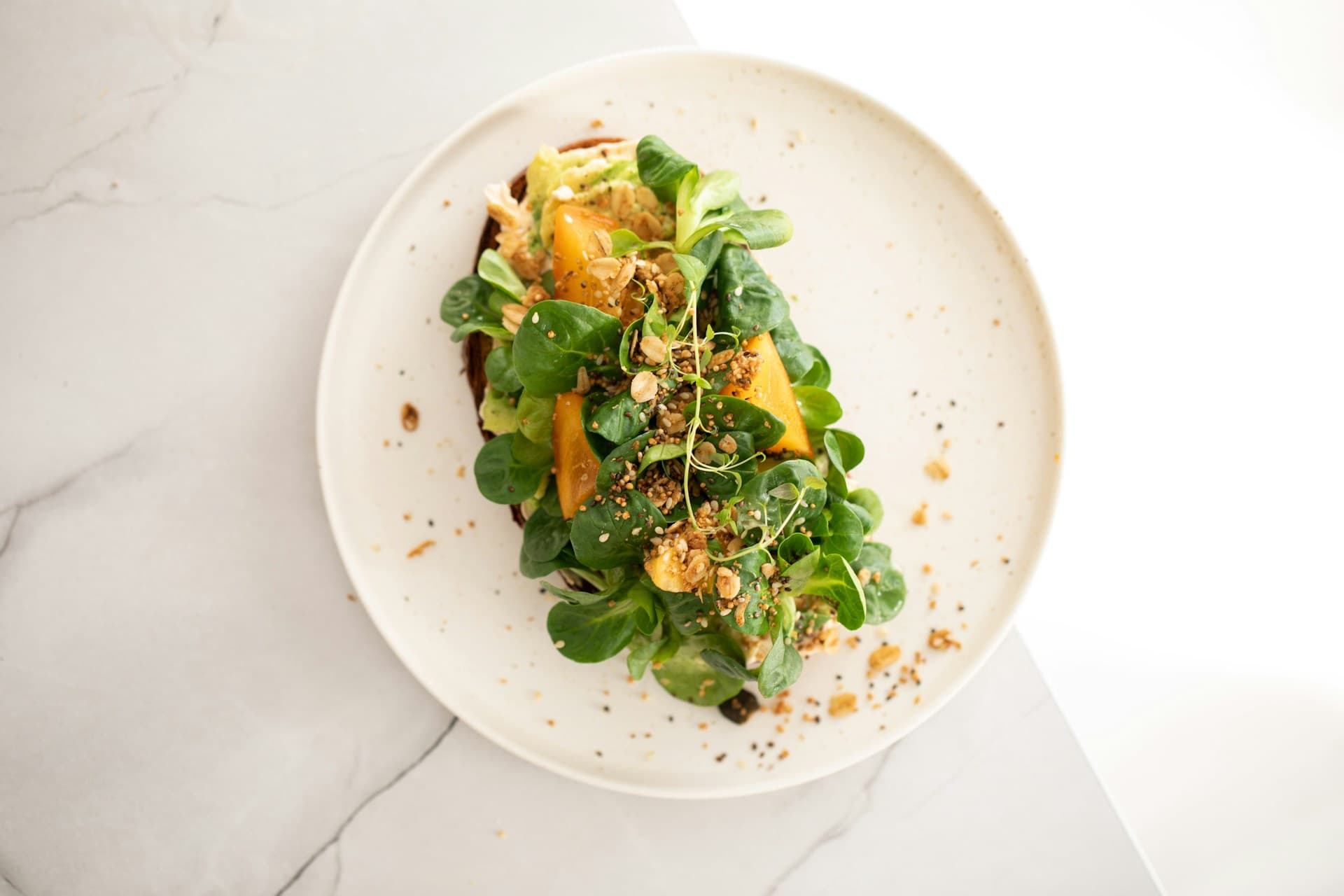 Top view of a plated fresh salad with greens and crumbled toppings on a white marble surface